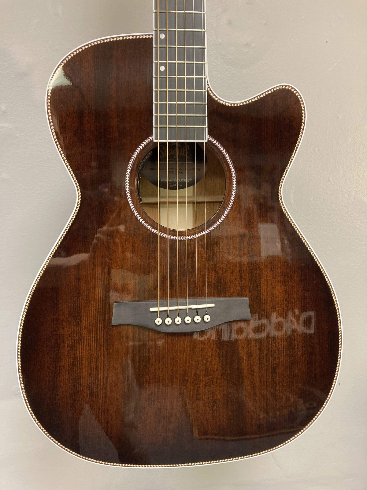 A close-up of the Seagull Artist Mosaic CH CW Acoustic-Electric Guitar in Bourbon Burst shows its glossy dark brown finish, white edge trim, and six strings, featuring the body and neck against a light background. Includes TRIC case.