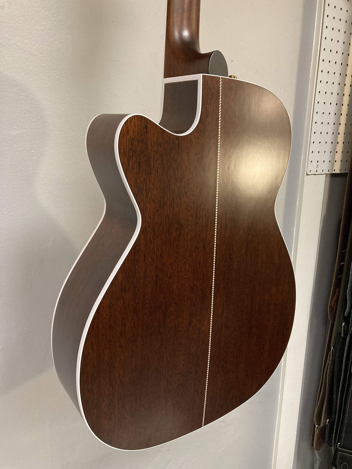 The image shows the back of a Seagull Artist Mosaic CH CW Acoustic-Electric Guitar - Bourbon Burst, featuring a smooth dark wood finish, white edge binding, and a decorative center inlay. The guitar is upright against a wall.