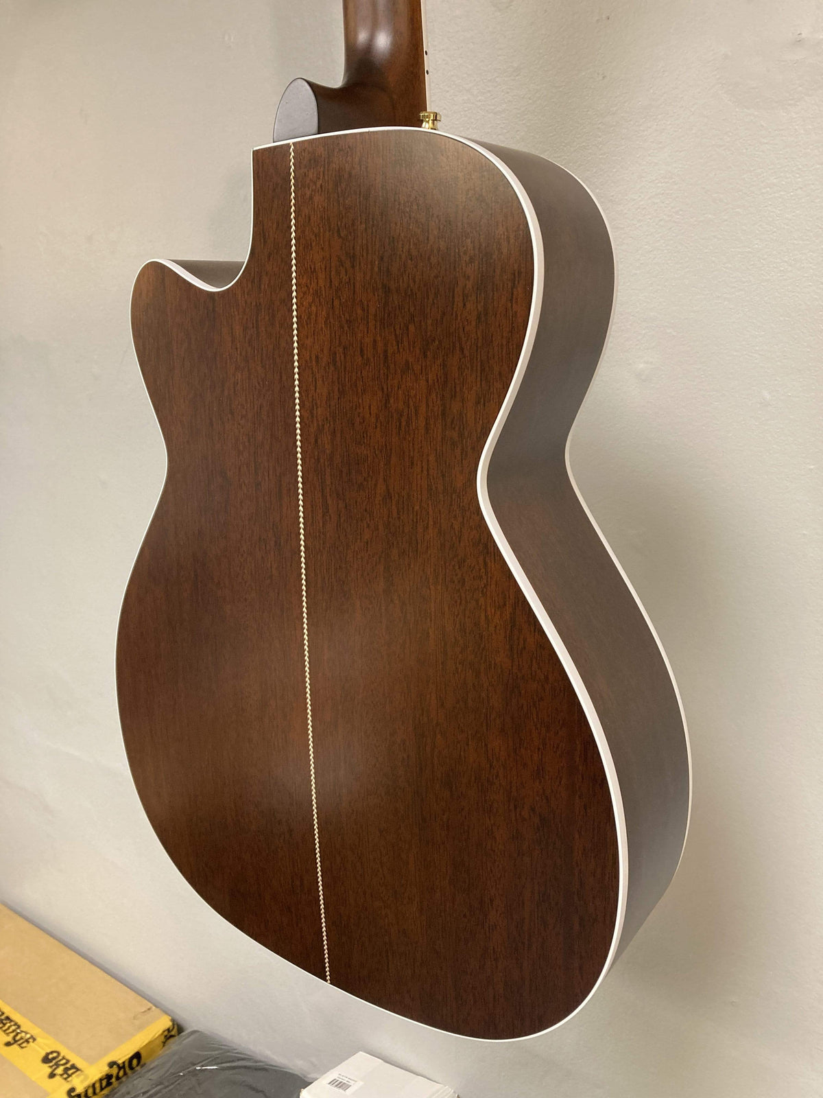 A close-up of the Seagull Artist Mosaic CH CW Acoustic-Electric Guitar - Bourbon Burst (with TRIC Case) shows its rich finish, white edge binding, and decorative center inlay as it rests against a light-colored wall.