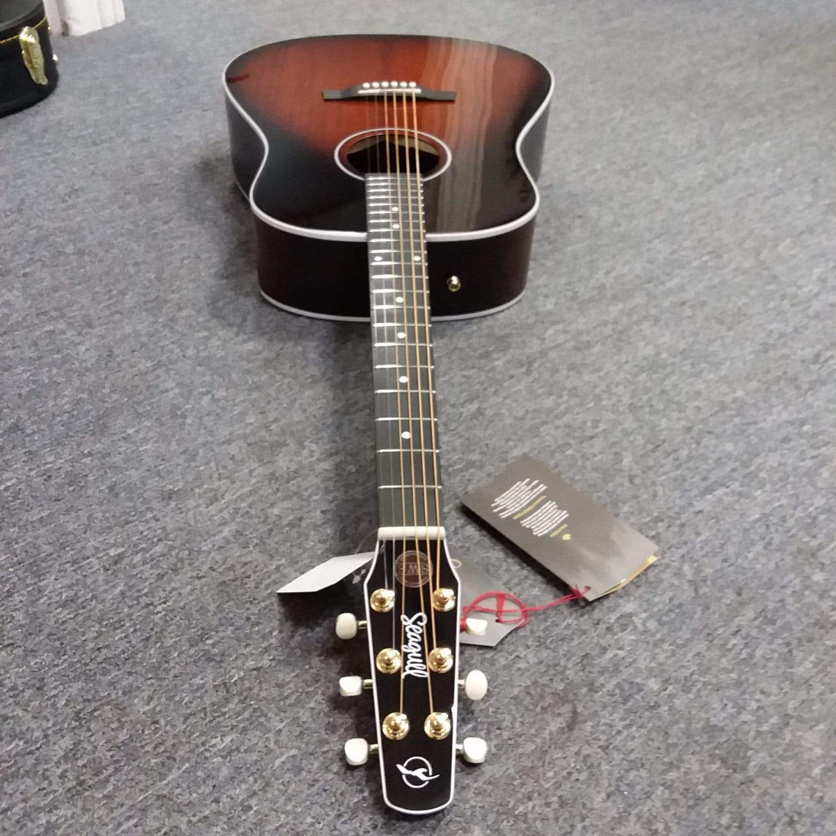 Seagull Maritime SWS Mahogany Burnt Umber GT QIT Acoustic Guitar lying on a grey surface, showcasing its elegant design and quality craftsmanship.