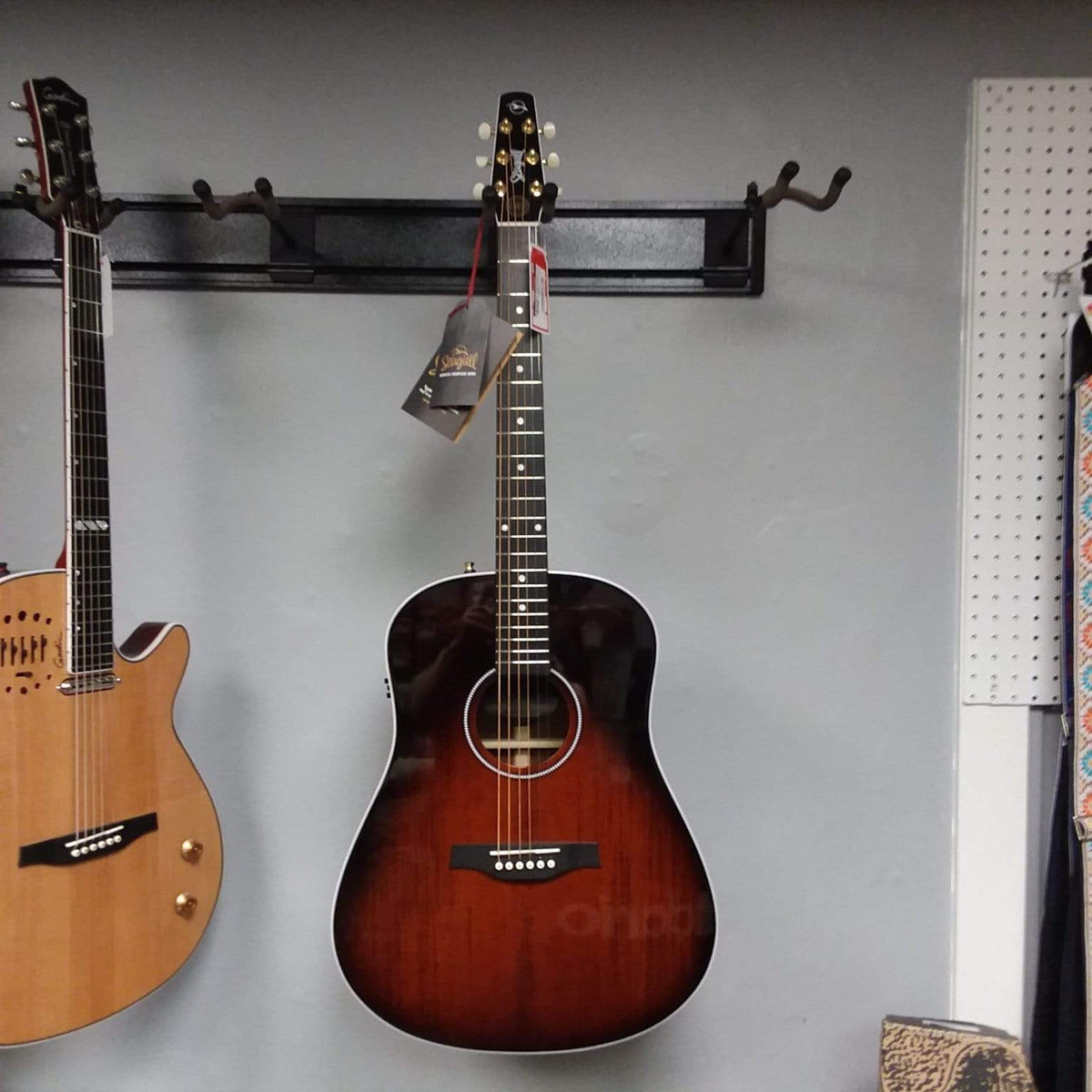Seagull Maritime SWS Mahogany Burnt Umber GT QIT Acoustic Guitar hanging on a wall, showcasing its elegant finish and detailed craftsmanship.