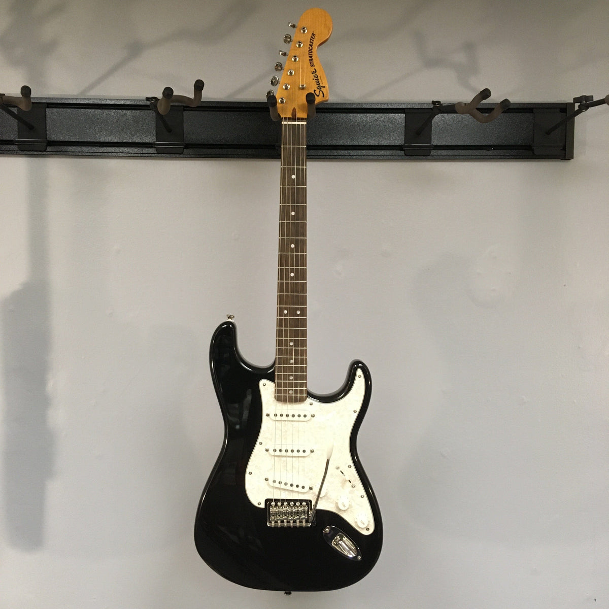 Squier Classic Vibe '70s Stratocaster Black Refurb, black and white electric guitar on a wall, showcasing vintage-style hardware and Fender-Designed alnico pickups.