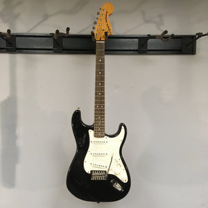 Squier Classic Vibe '70s Stratocaster Black Refurb, black and white electric guitar on a wall, showcasing vintage-style hardware and Fender-Designed alnico pickups.