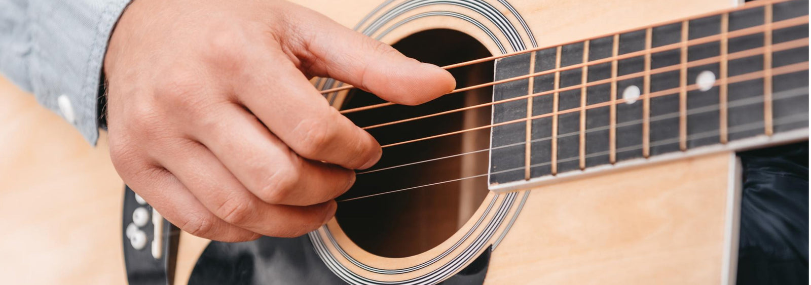 A person playing an acoustic guitar, focusing on the hand strumming strings. Perfect for a guitar store offering lessons and repairs.