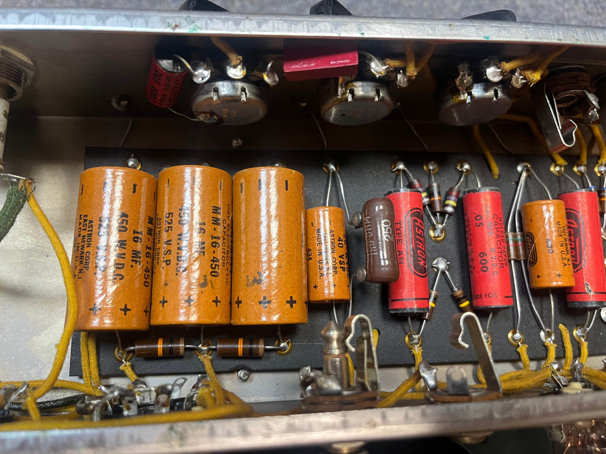 Close-up of electronic components, such as orange and red capacitors, resistors, and wires on the circuit board inside a 1954 Fender Tweed Deluxe Model 5D3 by Guitars on Main.