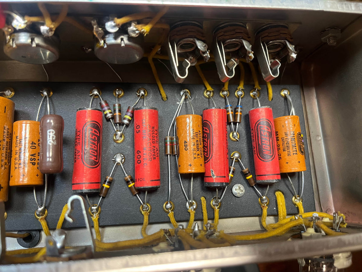 Close-up view of electronic components, like resistors and capacitors, inside a metal enclosure—typical of hand-wired amps such as the 1954 Fender Tweed Deluxe Model 5D3 w/Flight Case from Guitars on Main.