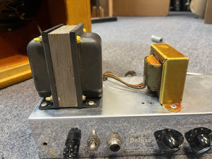 Close-up of electronic components, including a transformer and wiring, mounted on the metal chassis of a 1954 Fender Tweed Deluxe Model 5D3 w/Flight Case by Guitars on Main, resting on a carpeted surface.