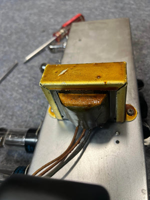 A close-up of the yellow wound transformer on a metallic chassis, surrounded by wires and parts in the Guitars on Main 1954 Fender Tweed Deluxe Model 5D3 w/Flight Case, shows classic hand-wired amp craftsmanship.