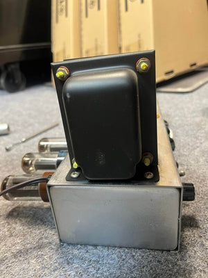 A close-up of the 1954 Fender Tweed Deluxe Model 5D3 by Guitars on Main, showing its vintage vacuum tubes and black metal parts on a silver chassis, resting on carpet.