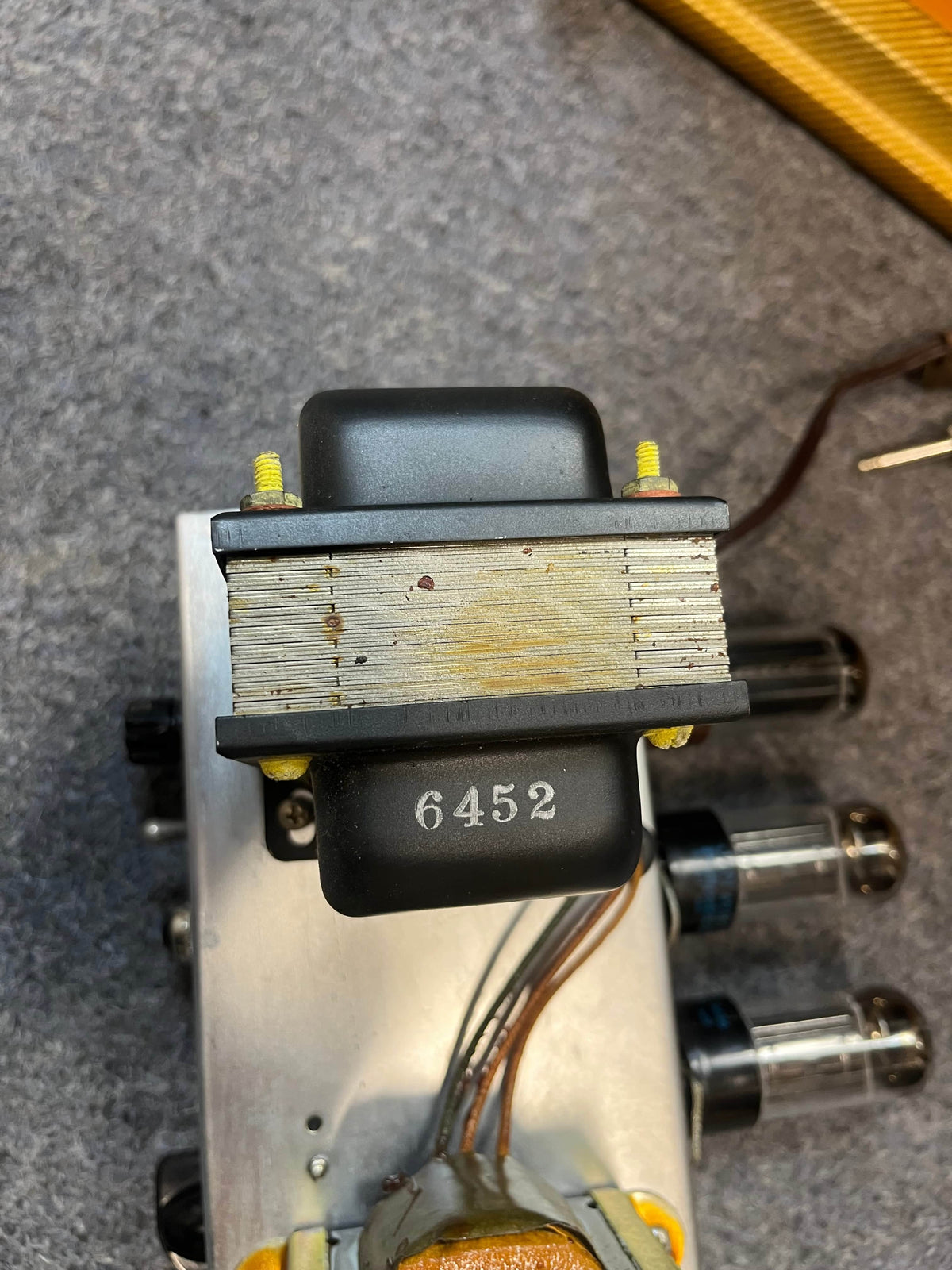 Close-up of a metal transformer marked 6452, mounted on a vintage Guitars on Main 1954 Fender Tweed Deluxe Model 5D3 tube amplifier chassis with visible wires and vacuum tubes, sold with flight case.