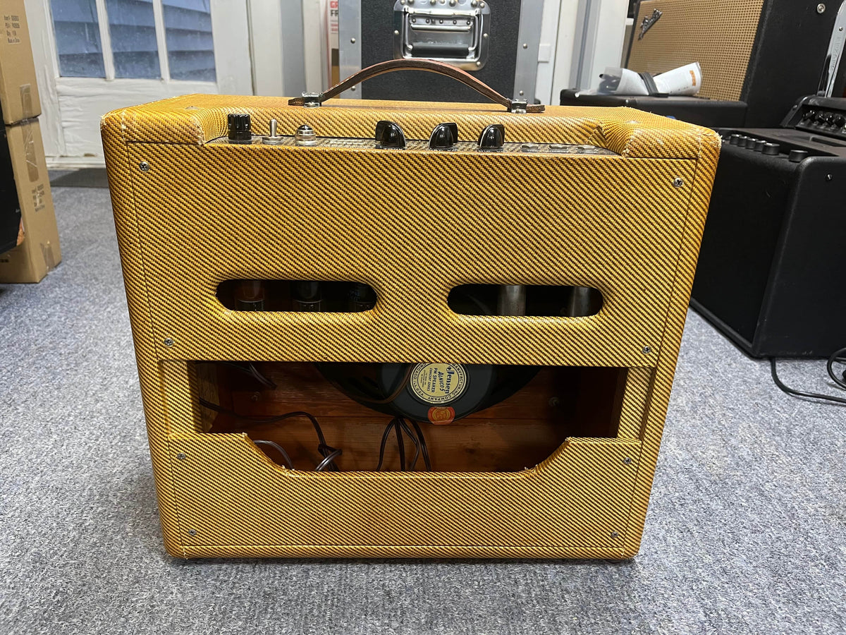 The 1954 Fender Tweed Deluxe Model 5D3 by Guitars on Main features a vintage tweed covering, open back, visible components, speaker, and comes with a flight case—all displayed on a carpeted floor.