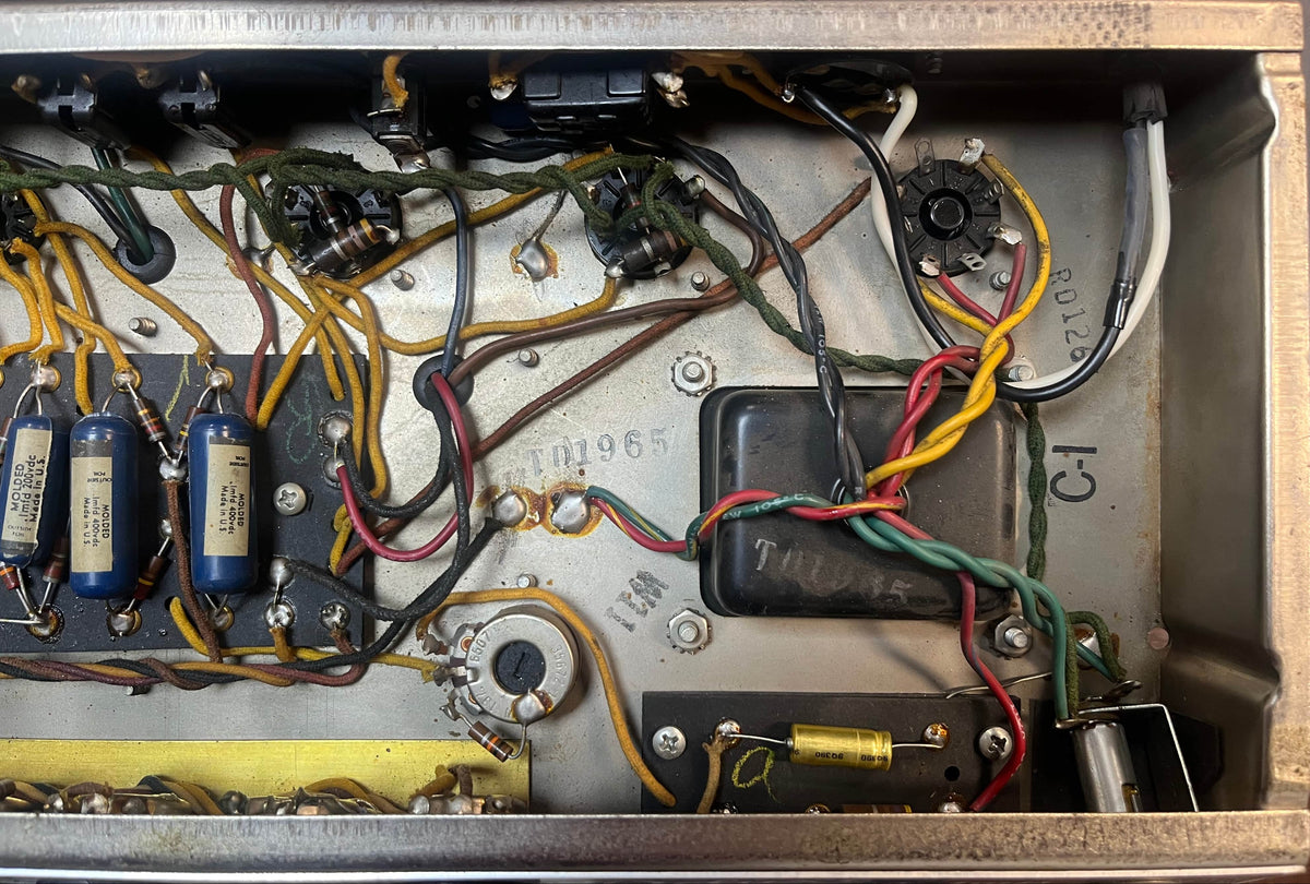 Close-up of vintage circuitry inside a metal enclosure, showing capacitors, resistors, wires, and connectors from a 1965 Fender Deluxe Reverb AB763 Pre-CBS Blackface amp, serial A 06439.