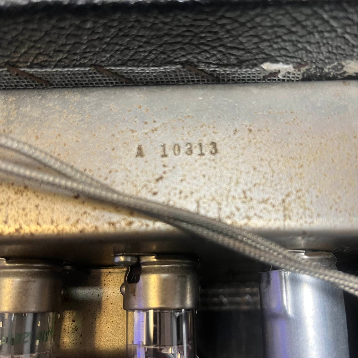 Close-up of a metallic surface stamped with "A 10313" above vacuum tubes and a cable, highlighting the iconic details of the 1965 Fender Super Reverb - Black Panel "Player’s Dream" Restoration by Guitars on Main.