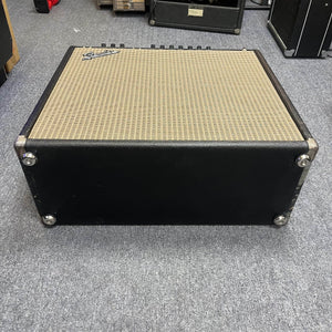 A 1965 Fender Super Reverb - Black Panel from Guitars on Main, this vintage black guitar amp with a beige grille is shown on a gray carpeted floor, viewed from the front and slightly above. Local pickup available.