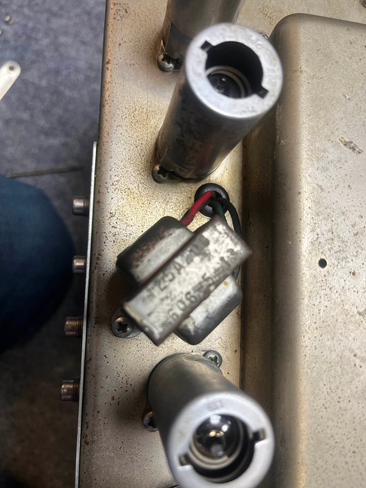 Close-up of a metallic component with wires, amid metal cylinders on a dusty surface—part of the 1965 Fender Super Reverb - Black Panel by Guitars on Main. Available for local pickup.