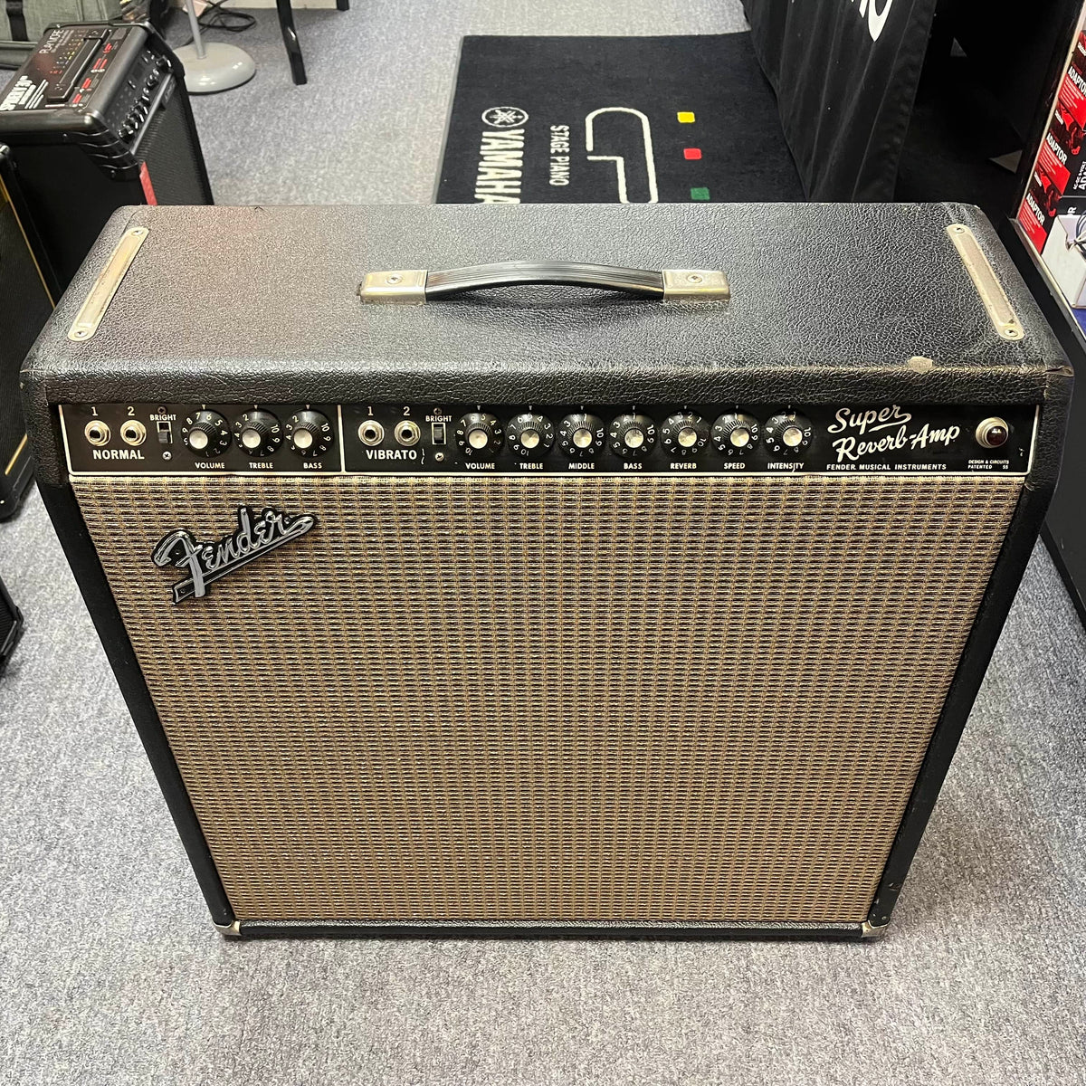 This 1965 Fender Super Reverb - Black Panel amp by Guitars on Main features top-panel knobs and switches, displayed on a carpeted floor in our music equipment store. Available for local pickup.