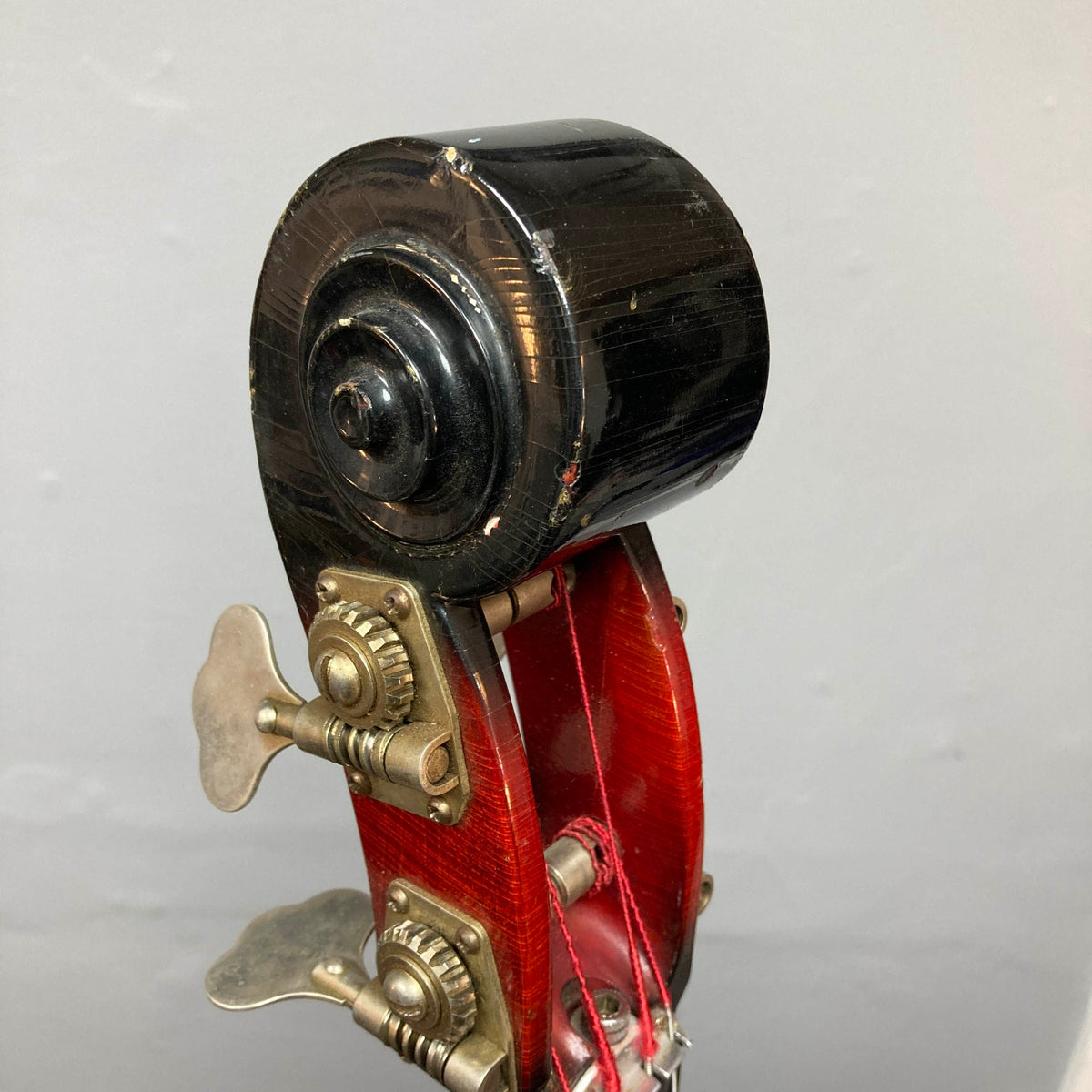 Close-up of the scroll and tuning pegs on an Ampeg 1966 ASB-1 Devil Bass (Serial #531), featuring red varnish and metal hardware reminiscent of a vintage upright, set against a plain gray background.