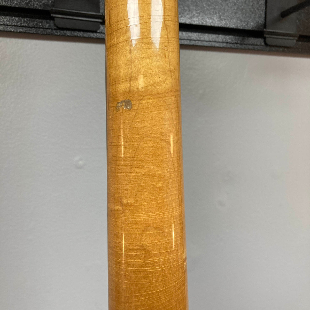 Close-up of the wooden neck of a 1966 Ampeg ASB-1 Devil Bass (Serial #531), showcasing pronounced grain patterns, minor scratches, and a small ding—details that highlight its vintage character—set against a plain light gray wall.