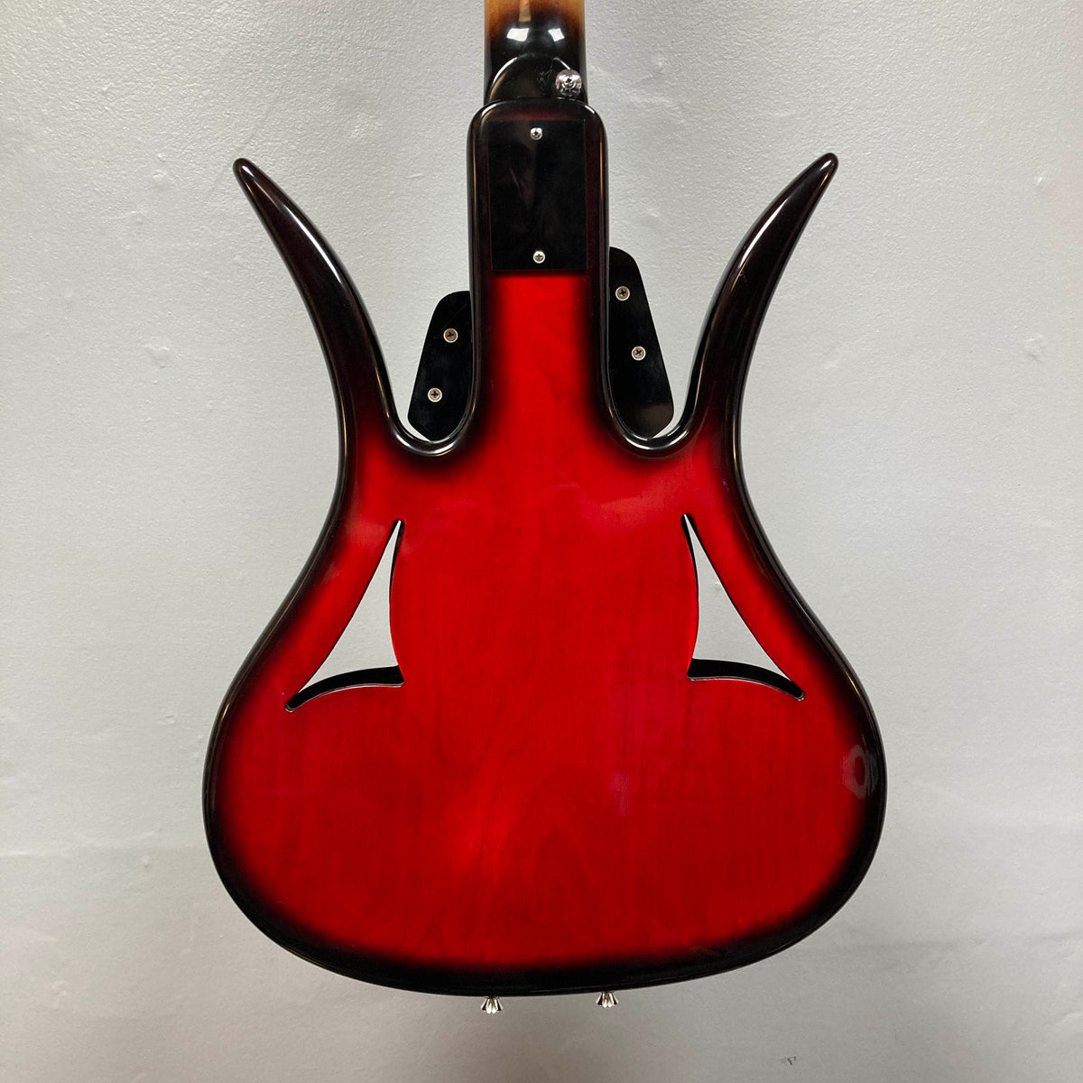 The back of an Ampeg 1966 ASB-1 Devil Bass (Serial #531) with a glossy red finish, distinctive curved horns, and two f-shaped sound holes is shown against a plain light-colored wall.
