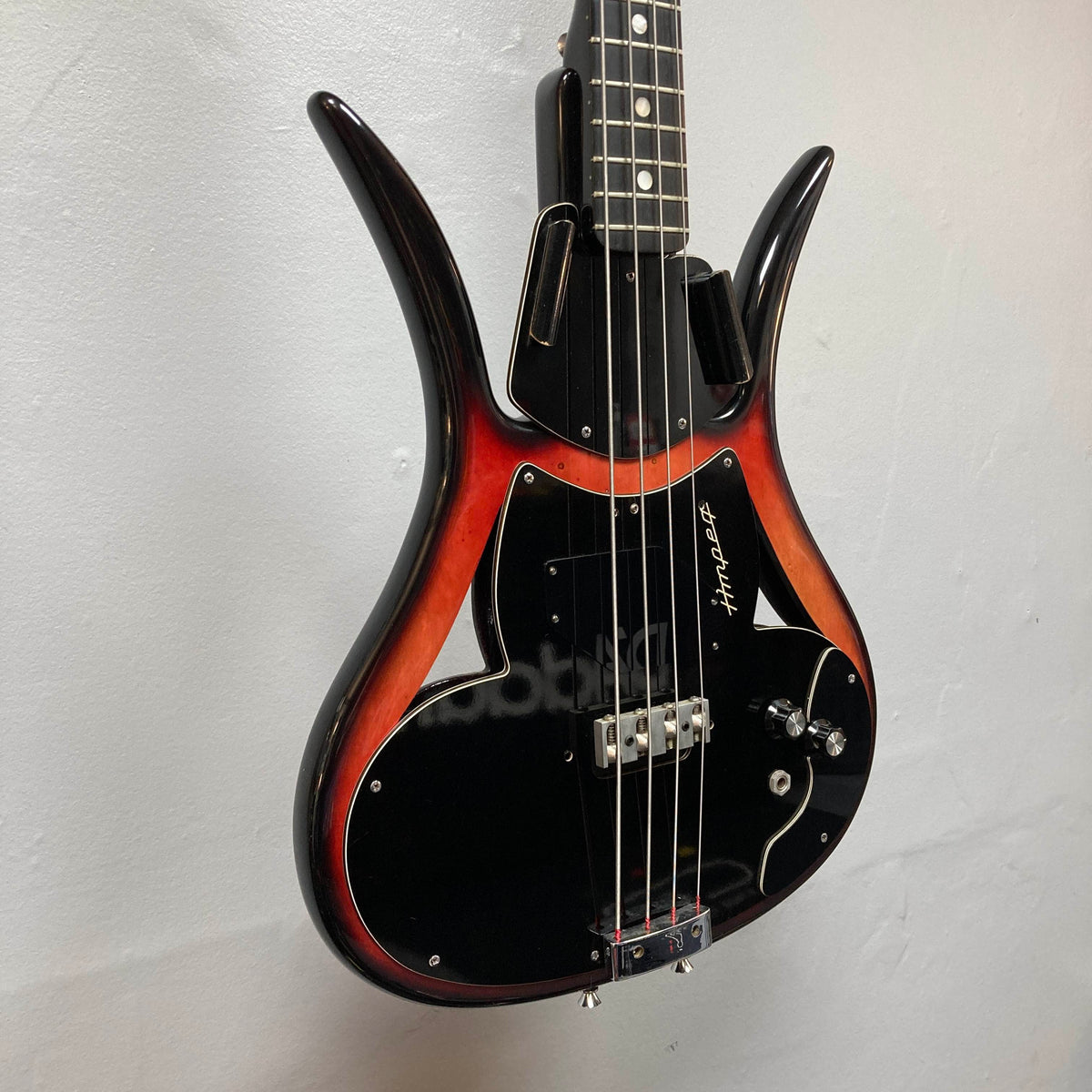 Vintage bass enthusiasts will appreciate the 1966 Ampeg ASB-1 Devil Bass Serial #531, featuring a striking sunburst and black finish, two pickups—including a distinctive bridge-mounted transducer pickup—and a signature on the pickguard, elegantly displayed on a light-colored wall.