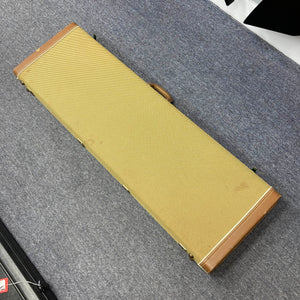 A rectangular, tan and brown hard Fender guitar case holding a 1966 Fender Jazz Bass Natural Refinish rests closed on a gray carpeted floor.