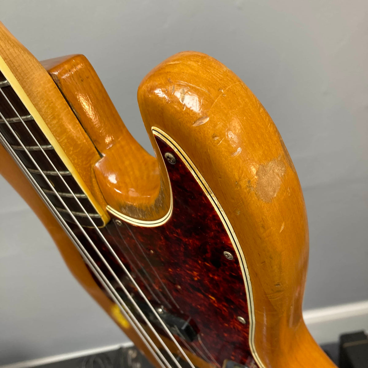 Close-up of a 1966 Fender Jazz Bass Natural Refinish by Fender, featuring visible scratches, dents, part of the neck, tortoiseshell pickguard, and original pickups; includes case.