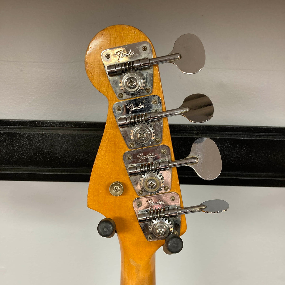 The image shows the back of a Fender 1966 Jazz Bass Natural Refinish headstock with four tuning pegs and Fender logos, highlighting this vintage bass guitar's classic design.