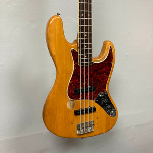 The 1966 Fender Jazz Bass Natural Refinish w/Case by Fender features a natural wood finish, tortoiseshell pickguard, visible wear below the strings, original pickups and knobs, hanging against a plain light-colored wall.