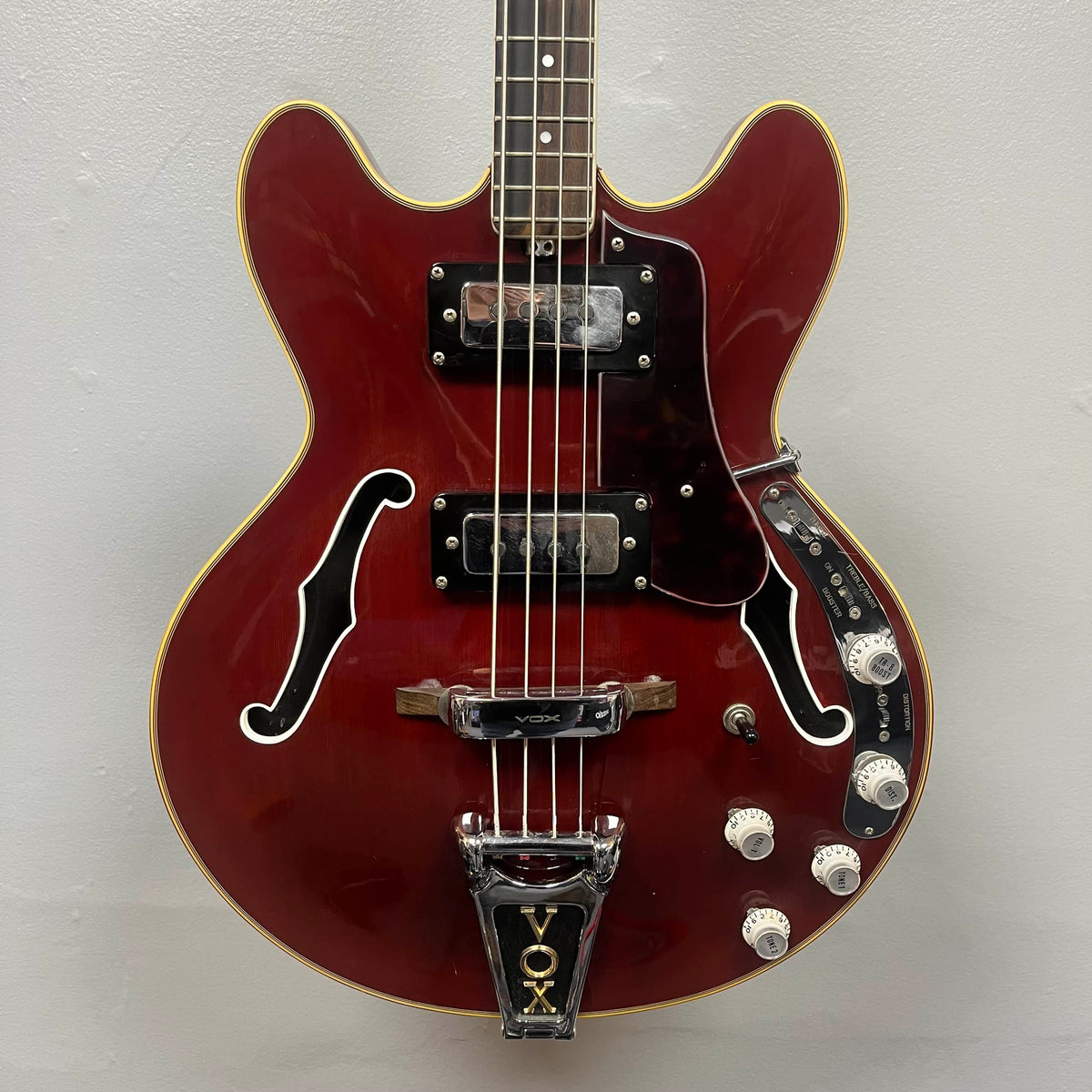 The 1967-68 Vox Sidewinder IV Bass (V272) Cherry by Vox is a red semi-hollow electric bass with two pickups, four white control knobs, and a VOX-marked Bigsby-style tremolo, echoing the classic vintage Italian design.