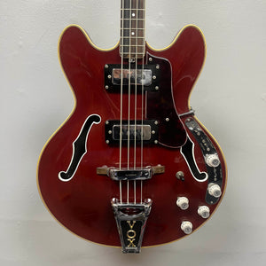 The 1967-68 Vox Sidewinder IV Bass (V272) Cherry by Vox is a red semi-hollow electric bass with two pickups, four white control knobs, and a VOX-marked Bigsby-style tremolo, echoing the classic vintage Italian design.