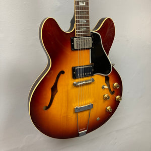 1967 Gibson ES-335 Sunburst electric guitar displayed on a wall, showcasing its vintage design and semi-hollow body craftsmanship, accompanied by a protective case.