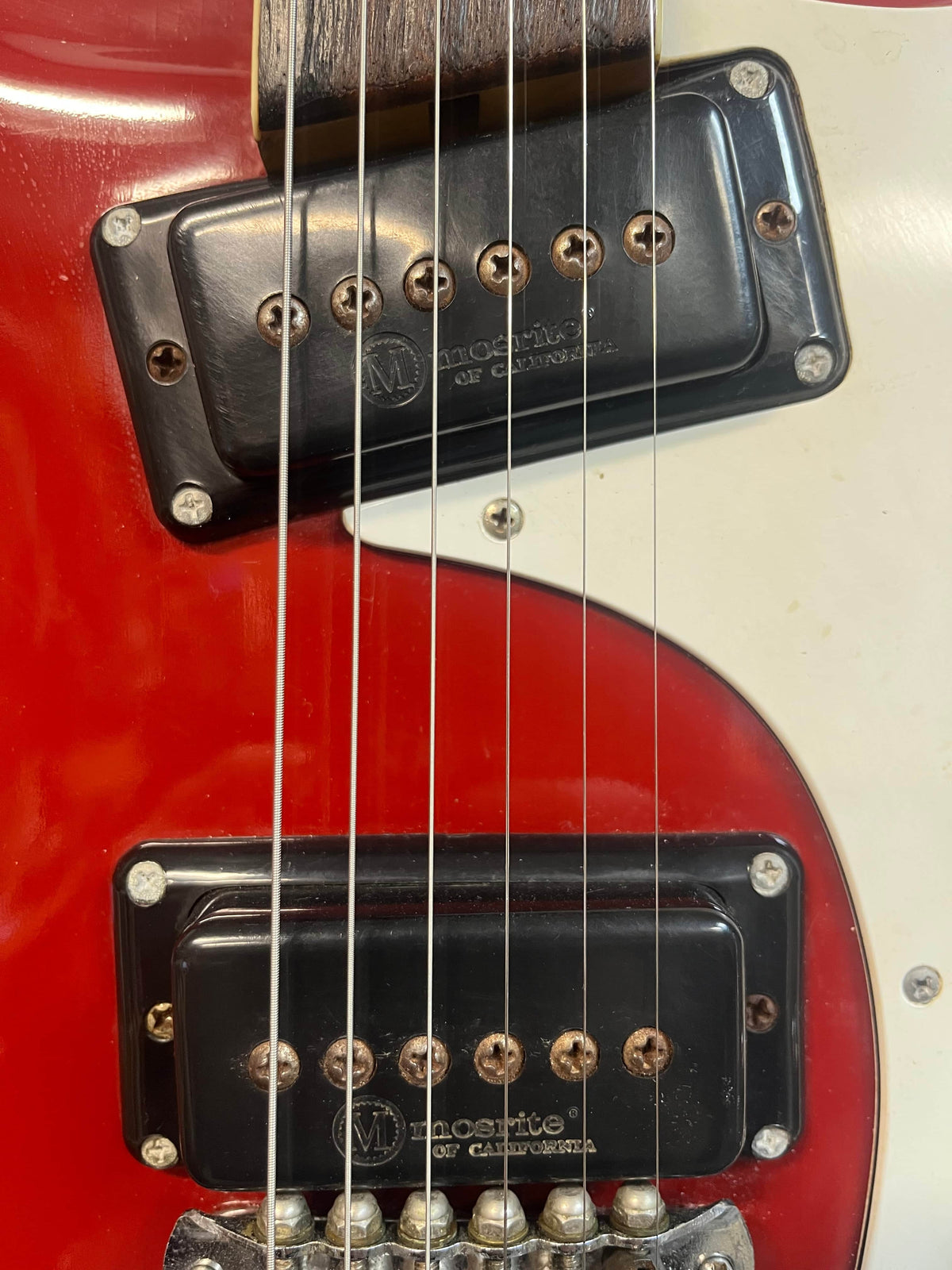 Close-up of a 1967 Mosrite Mark I Vintage Guitar by Mosrite, showing two black pickups labeled "Monolithic of California," part of the white pickguard, and six visible strings—highlighting classic American guitar heritage.