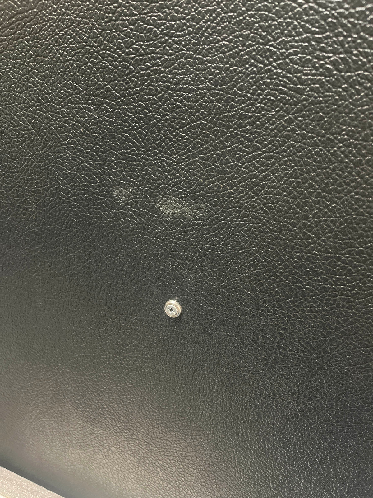 Close-up of a black textured surface—evocative of a vintage Marshall 1969 4x12 Cabinet with matching Celestion T1281 Greenbacks—featuring a small metal screw in the center and a faint smudge above it.