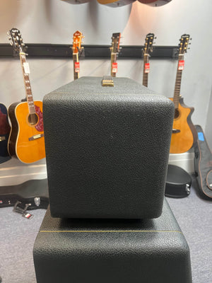 Close-up of a black, textured Marshall 1971 Lead Head JMP 1987 50 Watt amp with flight case, acoustic guitars hanging in the background, and guitar cases on the floor.