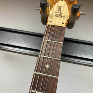 Close-up of the headstock of a 1975 Gibson Flying V w/Case by Gibson, showing part of the fretboard with six strings and a wall-mounted guitar hanger, featuring the iconic vintage Flying V design with a natural finish.