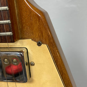 Close-up of a 1975 Gibson Flying V electric guitar with a natural finish, featuring part of the fretboard, a chrome pickup, cream-colored pickguard, and a screw on the wooden body—showcasing classic Gibson craftsmanship.