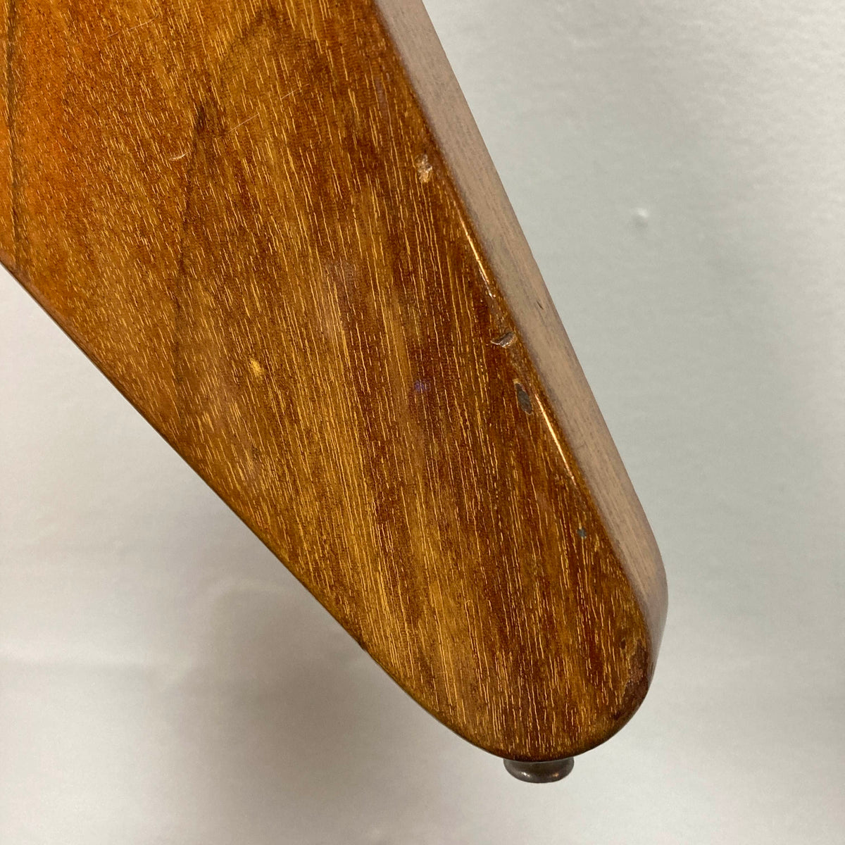 Close-up of a 1975 Gibson Flying V by Gibson with a glossy natural finish, showing some scratches and featuring a small round knob at the bottom, reminiscent of a vintage Flying V guitar, against a plain white background.