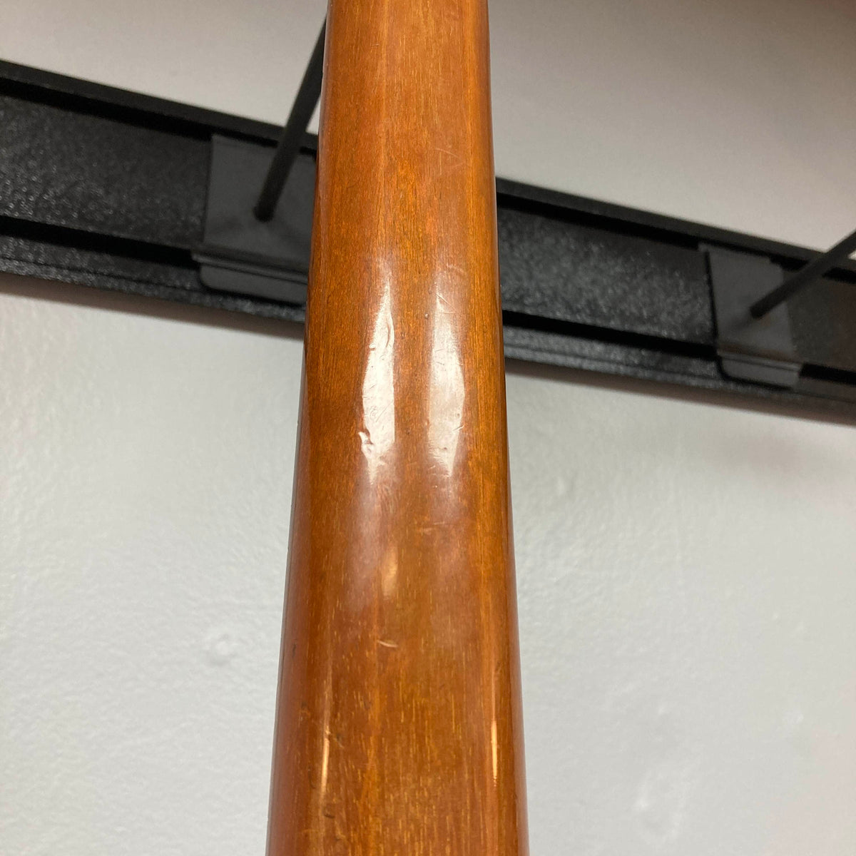 Close-up of the neck of a 1975 Gibson Flying V w/Case by Gibson, featuring a natural wood finish with visible indentations and minor scratches. Displayed against a white wall and black metal wall hanger, the wear enhances the vintage character distinctive to this classic instrument.