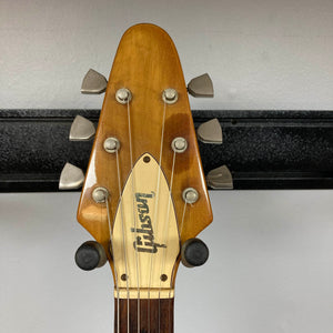 A close-up of the headstock of a 1975 Gibson Flying V w/Case by Gibson, featuring six tuning pegs, a natural finish, and the brand’s logo displayed on a metal plate.