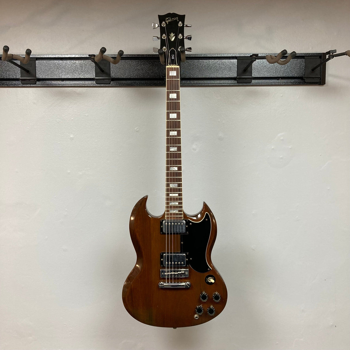 1975 Gibson SG Standard Walnut, electric guitar on a hook, showcasing its classic design and detailed fretboard inlays, available with a case.