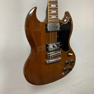 1975 Gibson SG Standard Walnut electric guitar with case, featuring beveled Honduran Mahogany body and detailed fretboard inlays, displayed on a wall.