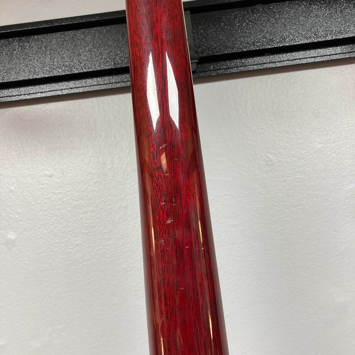 Close-up of the 1977 Gibson SG Standard Cherry by Gibson, its red glossy neck bearing visible scratches—set against a white wall and black horizontal rack, evoking the craftsmanship of the celebrated Kalamazoo era.