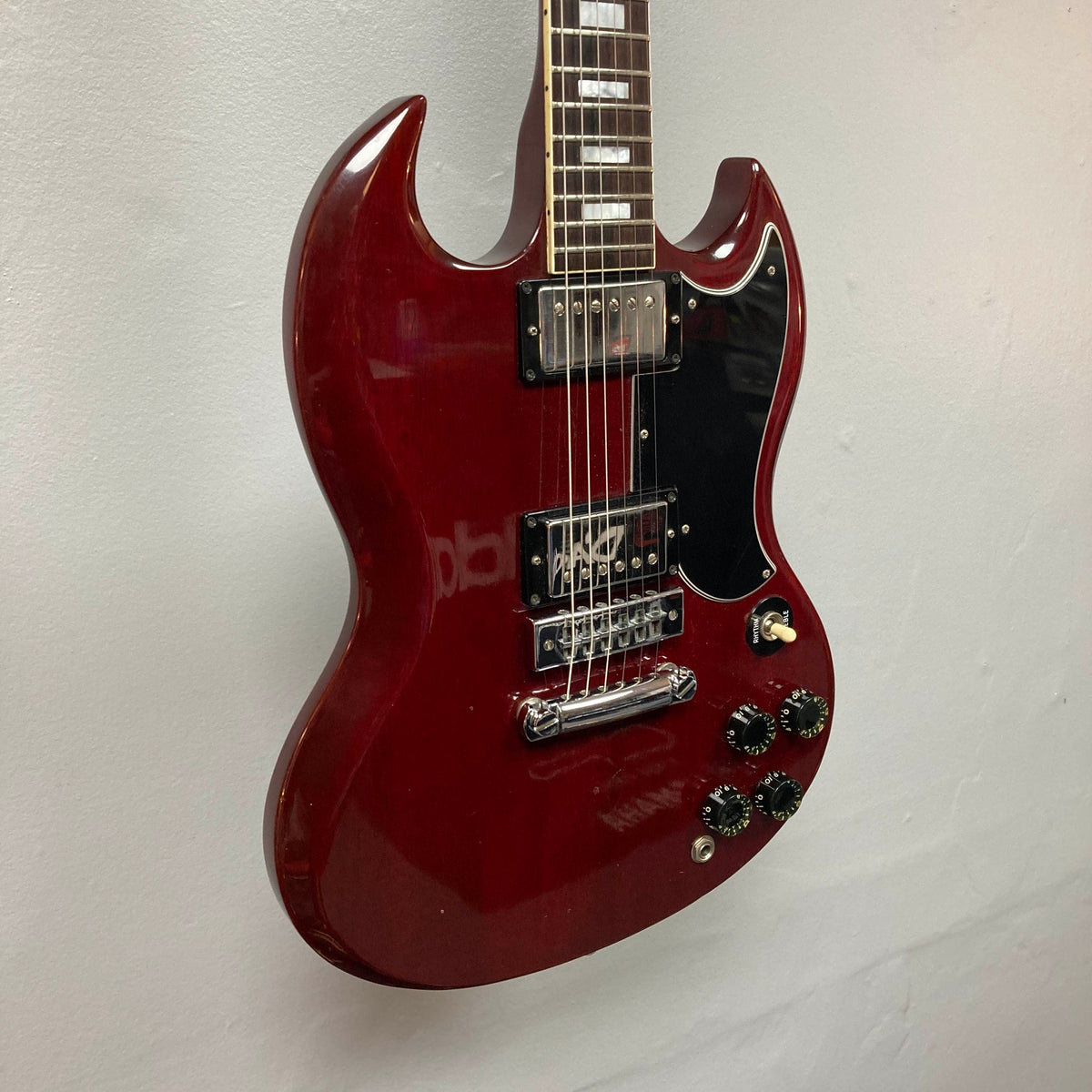 A 1977 Gibson SG Standard Cherry electric guitar by Gibson, featuring a double-cutaway mahogany body, two humbucker pickups, four control knobs, and a black pickguard, displayed against a white wall—a genuine classic from the iconic Kalamazoo era, complete with its original case.