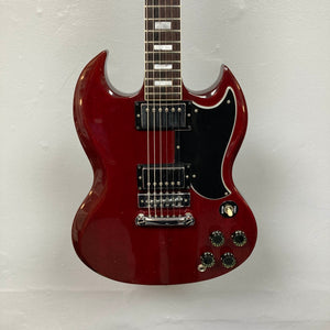 A 1977 Gibson SG Standard Cherry electric guitar by Gibson, featuring a classic double-cutaway mahogany body, two humbucker pickups, four control knobs, and a black pickguard evocative of the iconic Kalamazoo era, hangs elegantly against a plain white wall.