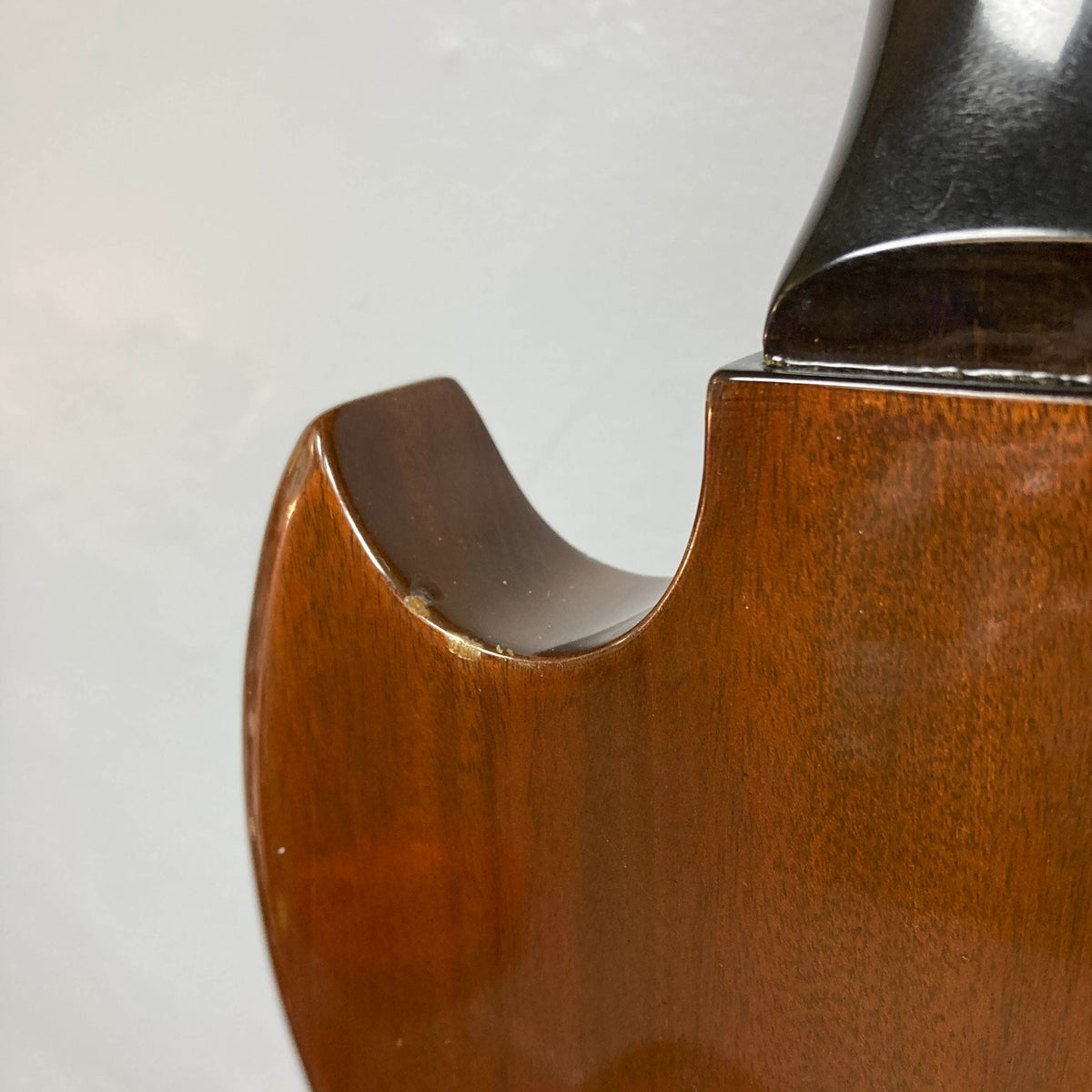 Close-up of a wooden string instrument, its curved edge and part of the neck displayed against a plain light-colored background—a composition reminiscent of classic instruments such as the 1978 Gibson EDS-1275 Double Neck Walnut w/Case by Gibson.