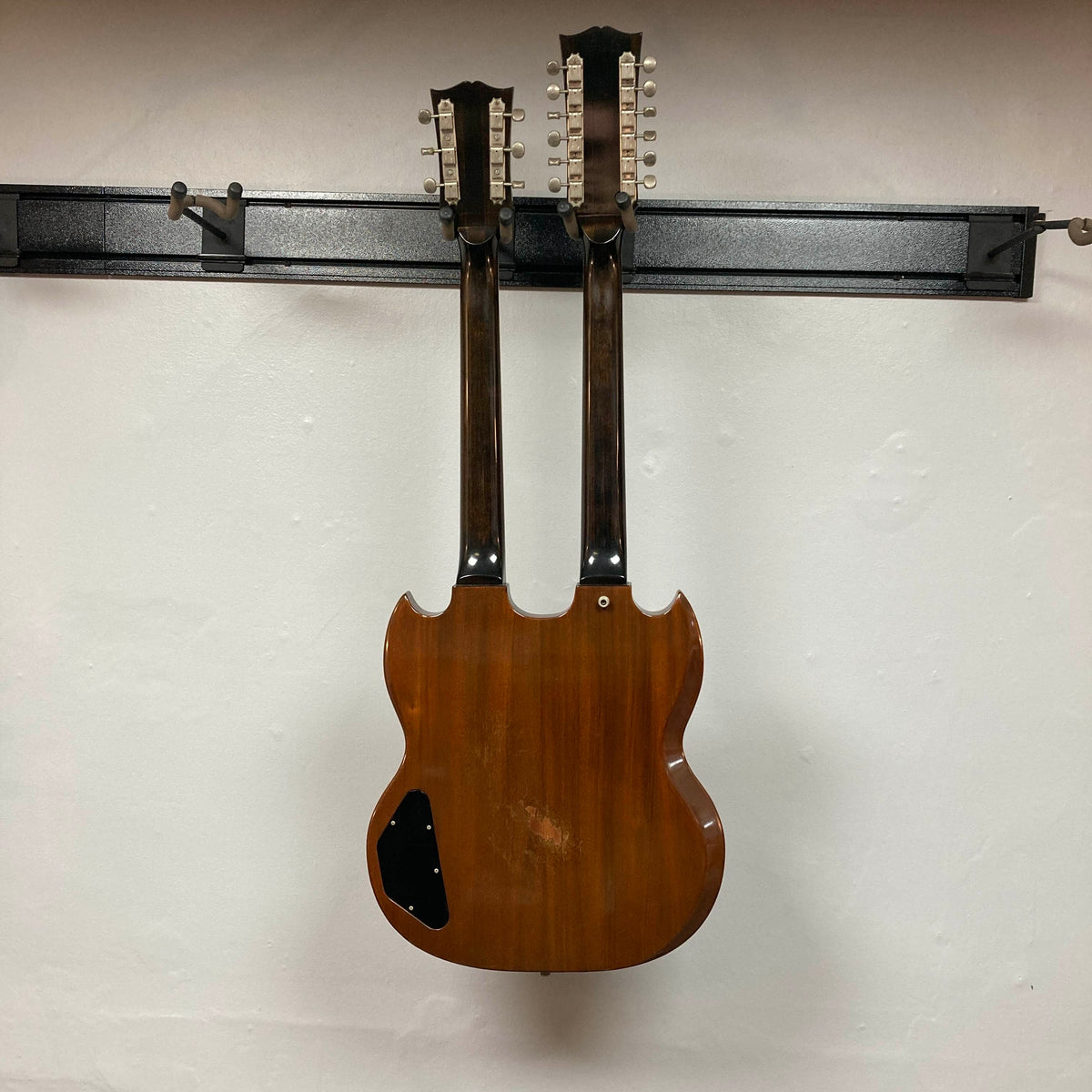 A 1978 Gibson EDS-1275 Double Neck Walnut guitar by Gibson hangs on a wall-mounted rack against a plain white background.