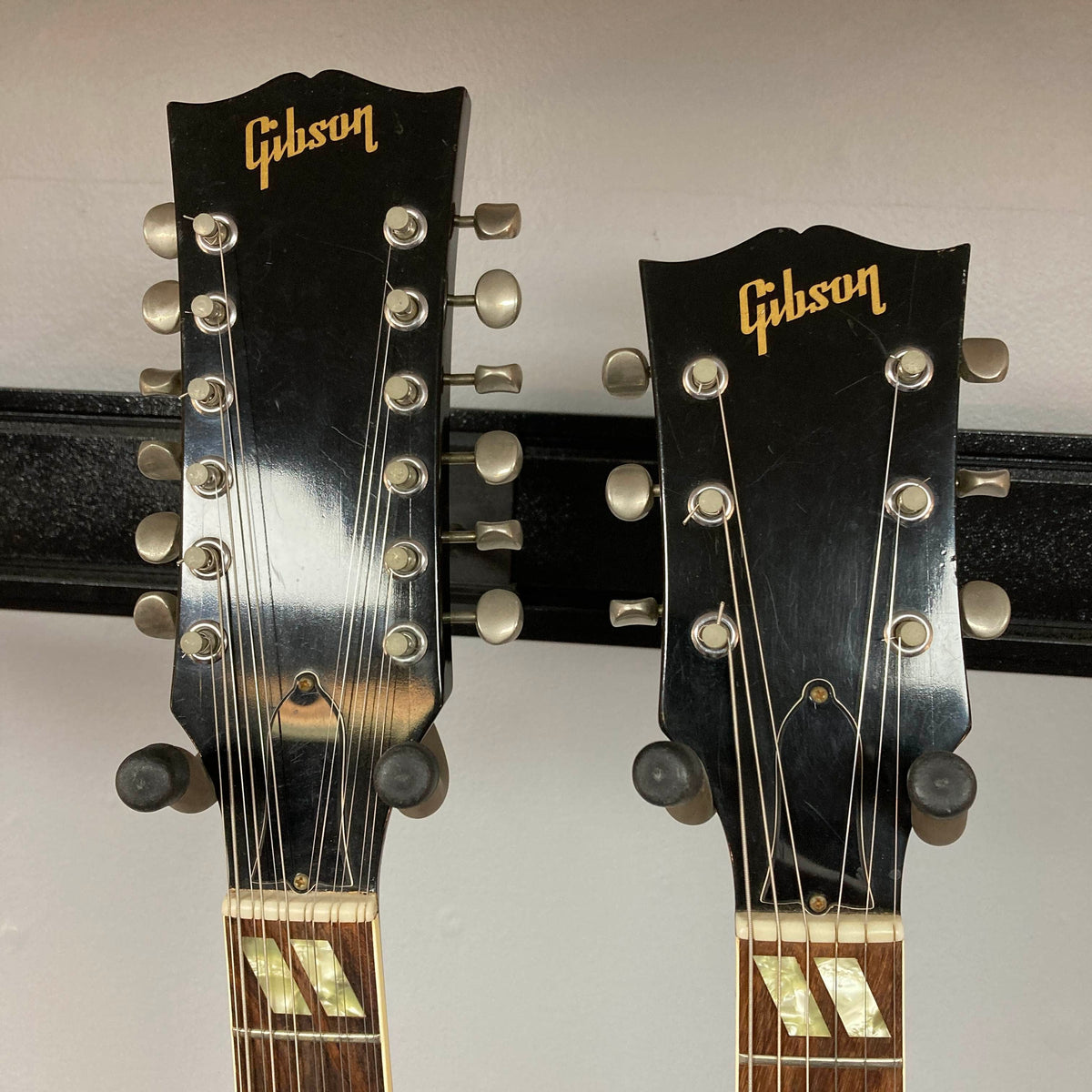 Two Gibson headstocks sit side by side: both from a 1978 Gibson EDS-1275 Double Neck Walnut w/Case. One features twelve tuning pegs for the 12-string neck, while the other has six tuning pegs for the 6-string neck. Both display the iconic gold Gibson logo.