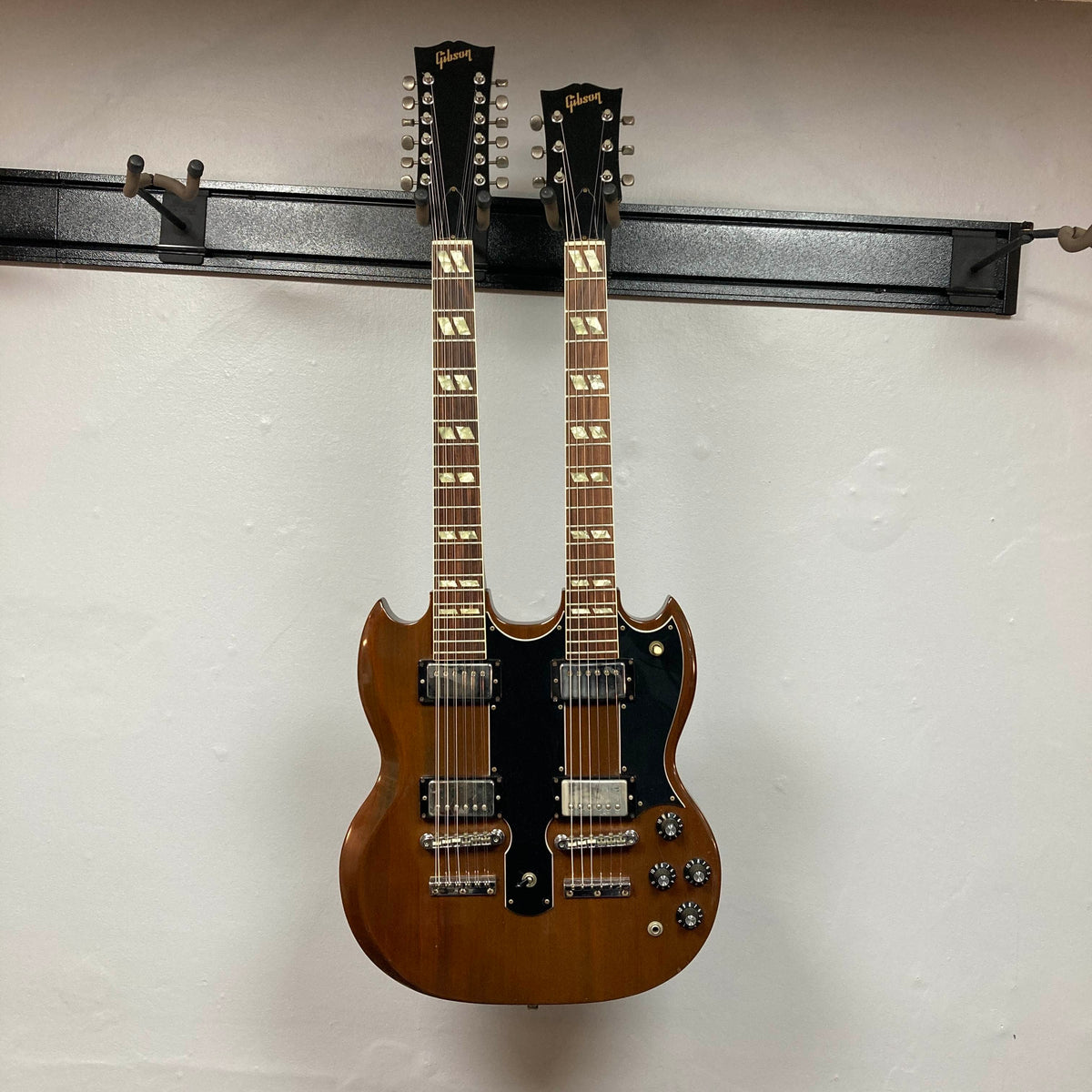 A 1978 Gibson EDS-1275 Double Neck Walnut w/Case by Gibson is mounted on a black wall rack against a plain white wall.