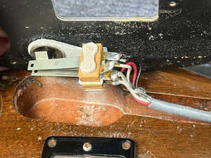 Close-up of the internal wiring of a 1978 Gibson EDS-1275 Double Neck Walnut w/Case by Gibson, displaying a switch, metal contacts, various wires, and a routed wooden cavity with visible dust and residue.