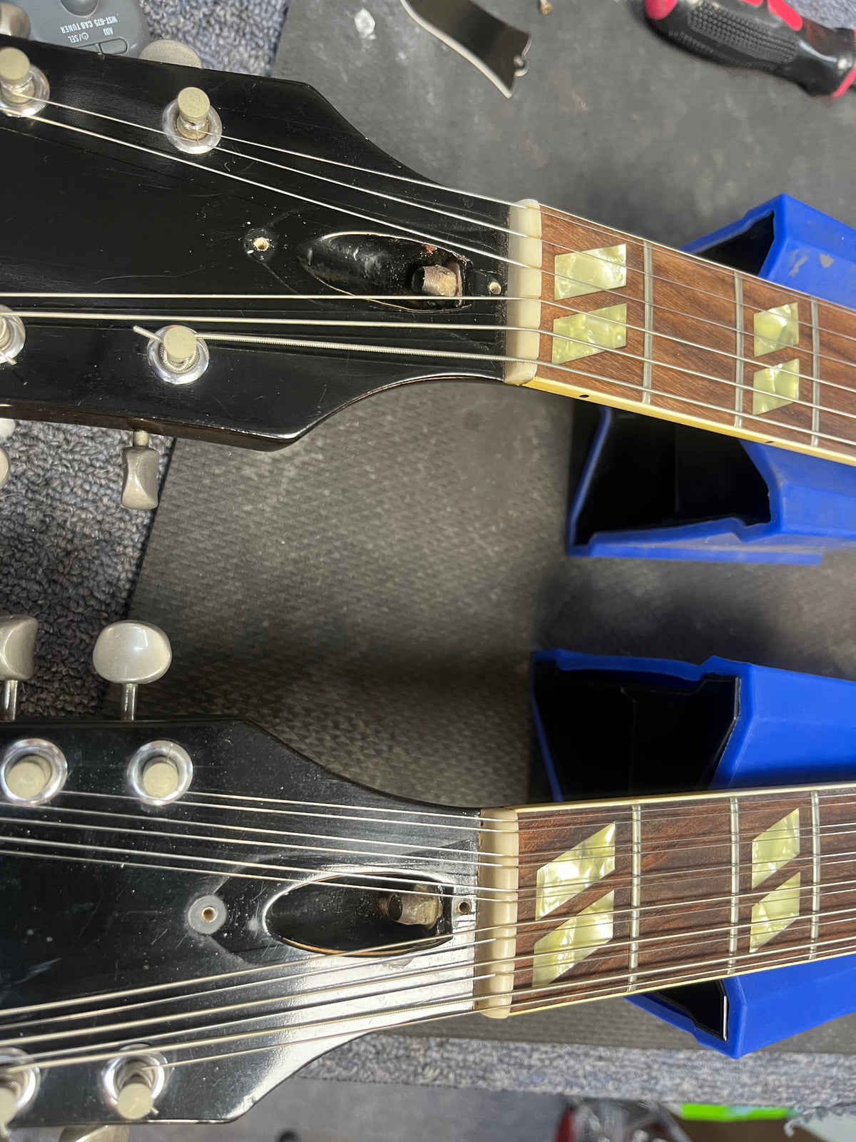 Two guitar necks placed side by side on a workbench, each supported by blue stands, showcasing the headstocks, tuners, and fretboards—reminiscent of the 1978 Gibson EDS-1275 Double Neck Walnut w/Case from Gibson.